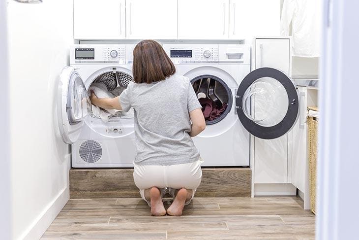 Femme accroupie devant un lave-linge et un sèche-linge